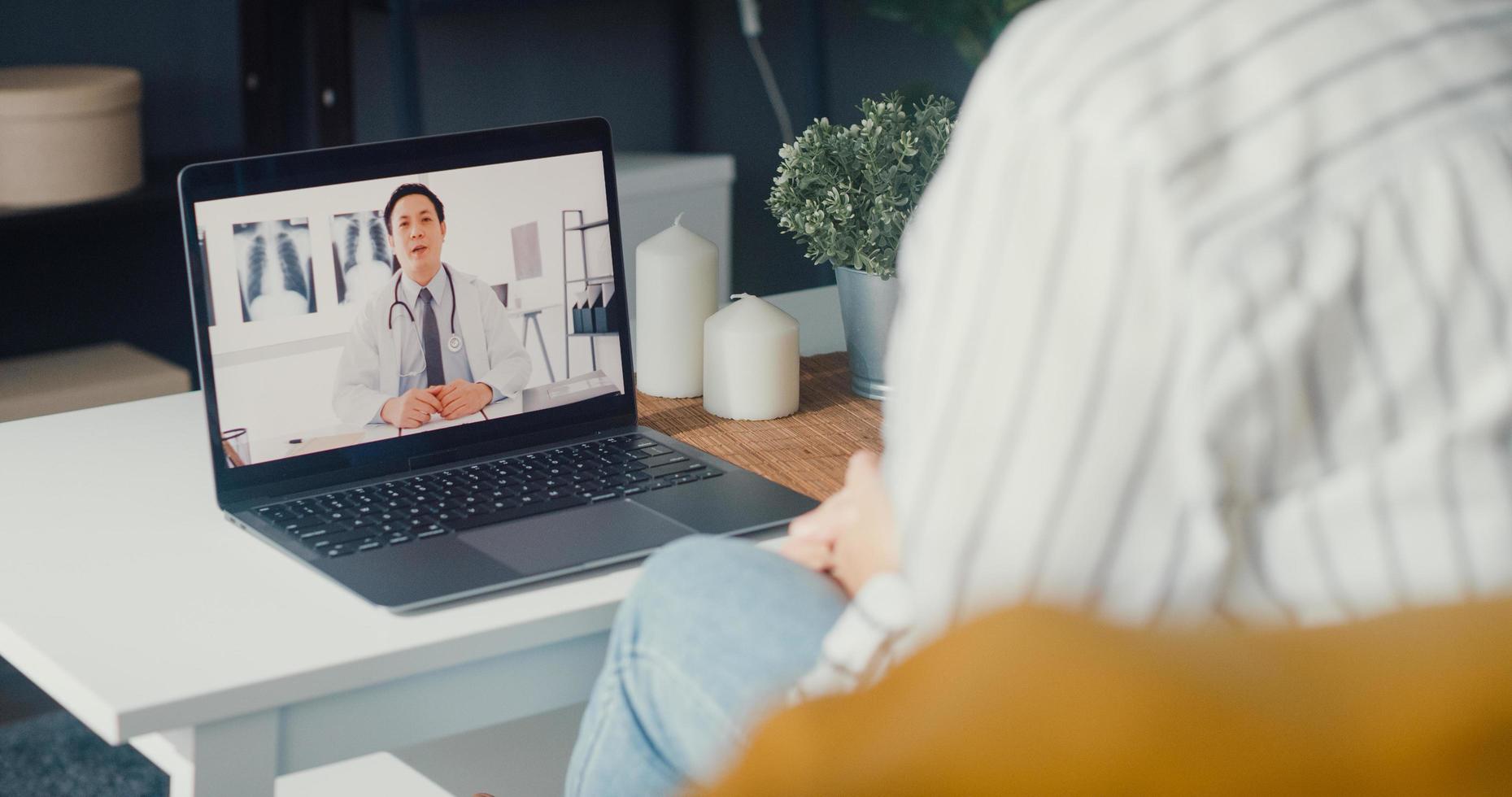 la giovane ragazza asiatica che utilizza il computer portatile parla della malattia in videoconferenza con la consultazione online di un medico senior nel soggiorno di casa foto