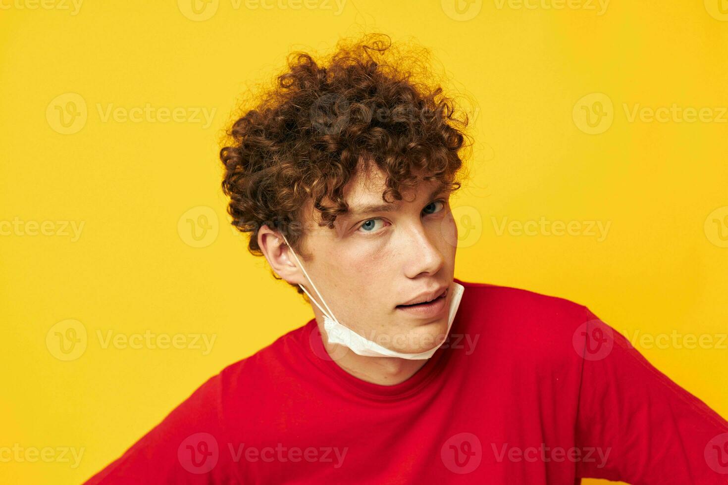 tipo con rosso Riccio capelli nel un' rosso maglietta medico maschera protezione giallo sfondo inalterato foto