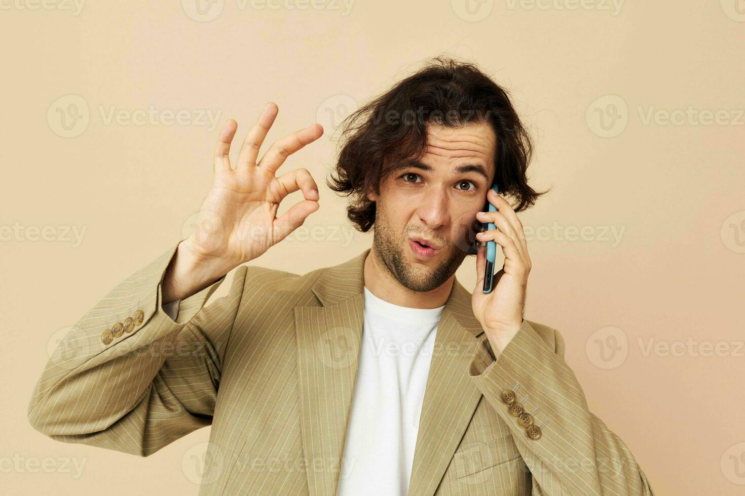 allegro uomo nel un' completo da uomo in posa emozioni parlando su il Telefono beige sfondo foto
