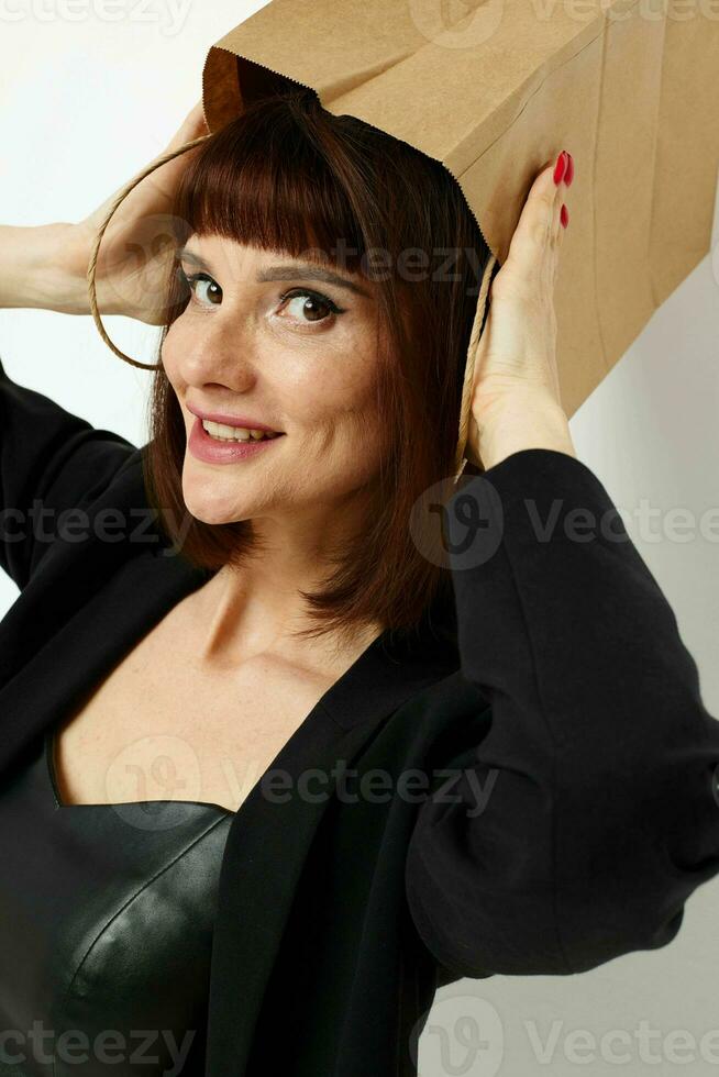 ritratto di un' donna nel un' pelle completo da uomo nero giacca con un' Borsa su il suo testa leggero sfondo foto
