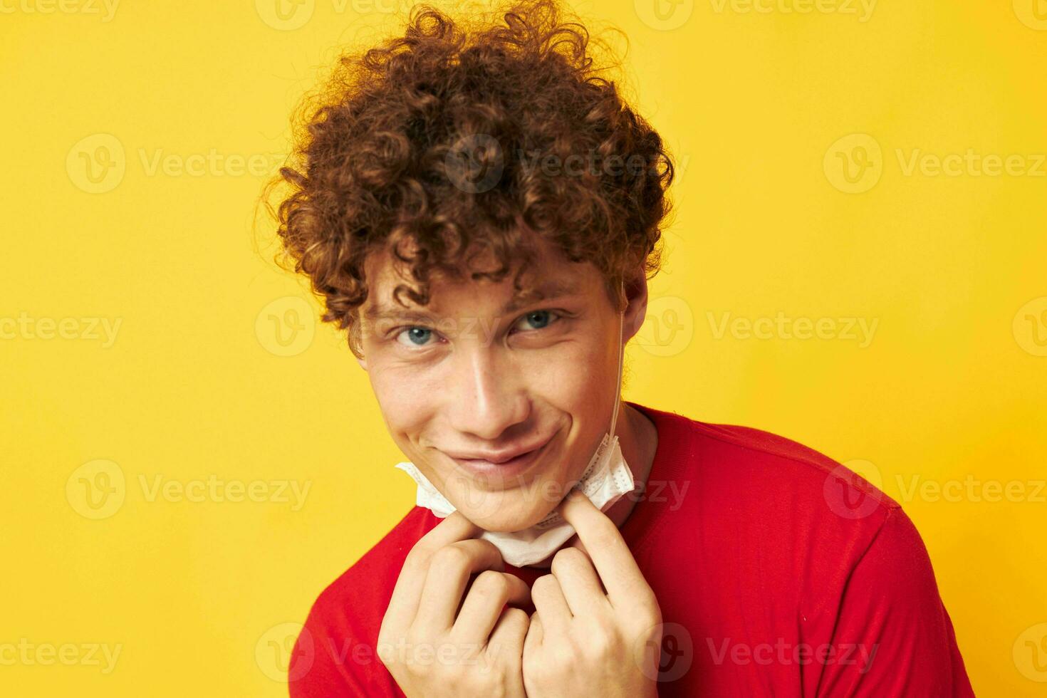 tipo con rosso Riccio capelli nel un' rosso maglietta medico maschera protezione giallo sfondo inalterato foto