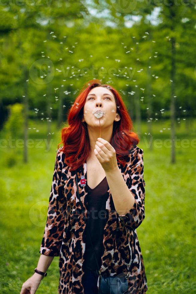 la giovane donna dai capelli rossi soffia via un dente di leone foto