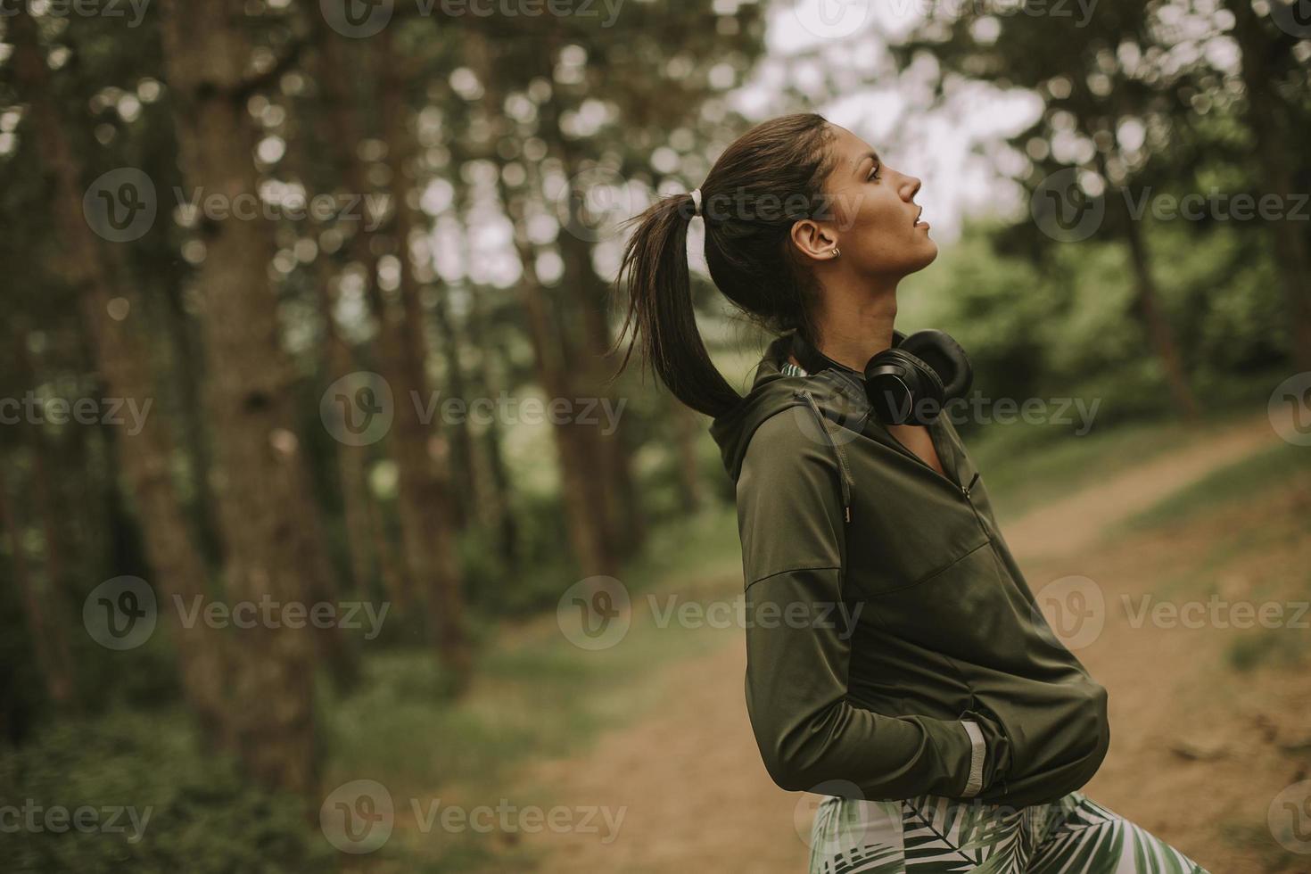 giovane corridore femminile bello ascoltare musica e fare una pausa dopo aver fatto jogging in una foresta foto