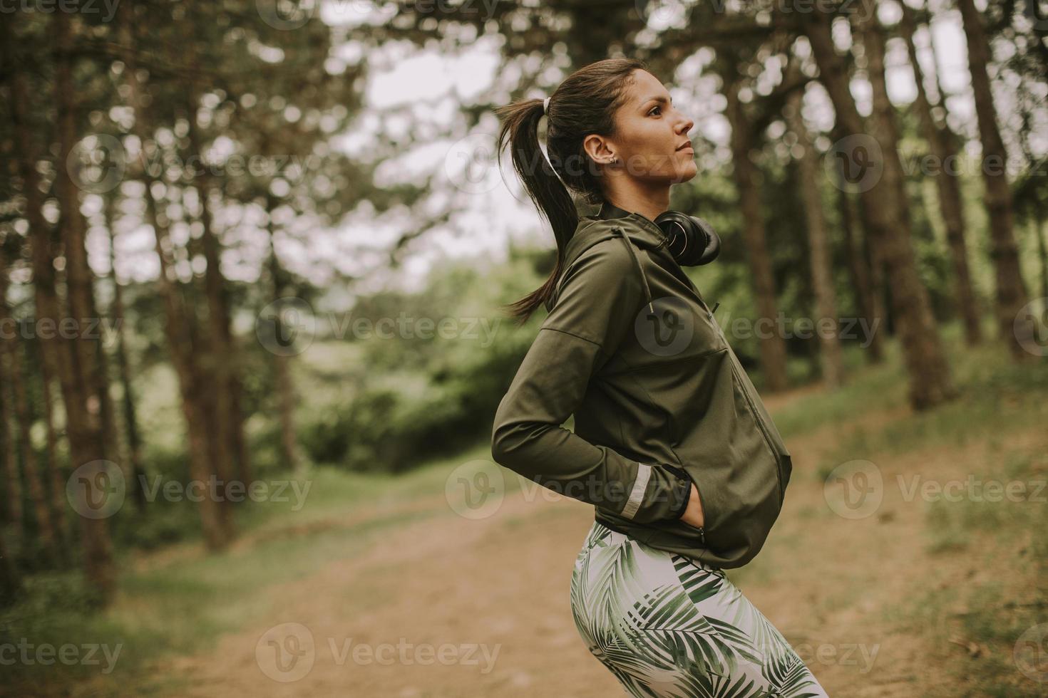 giovane corridore femminile bello ascoltare musica e fare una pausa dopo aver fatto jogging in una foresta foto