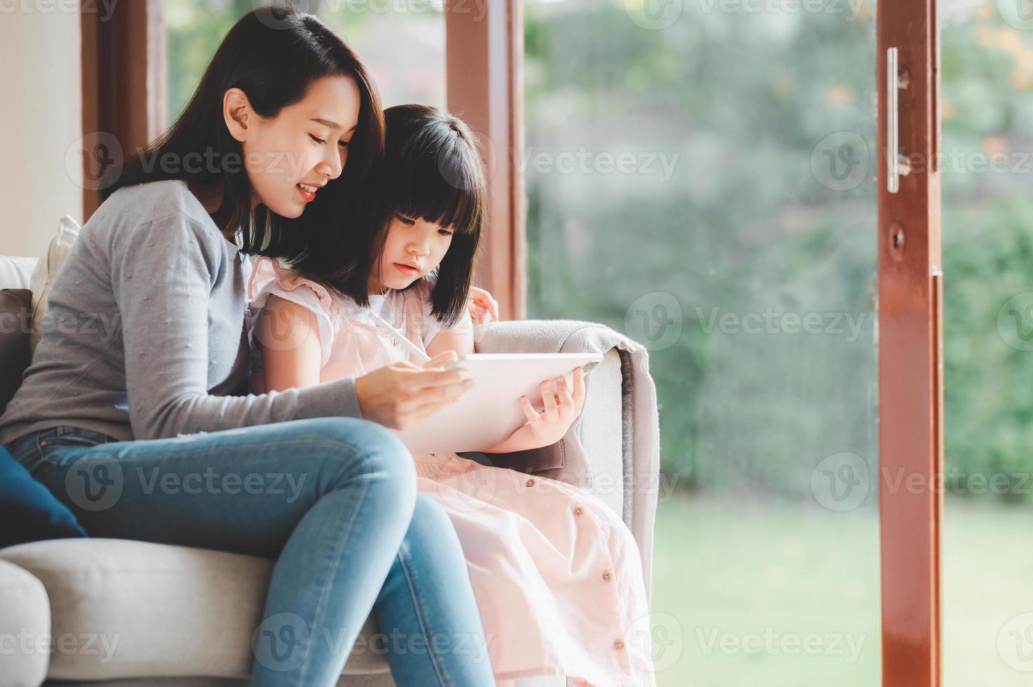 famiglia asiatica felice che usa la tavoletta digitale per studiare insieme a casa foto