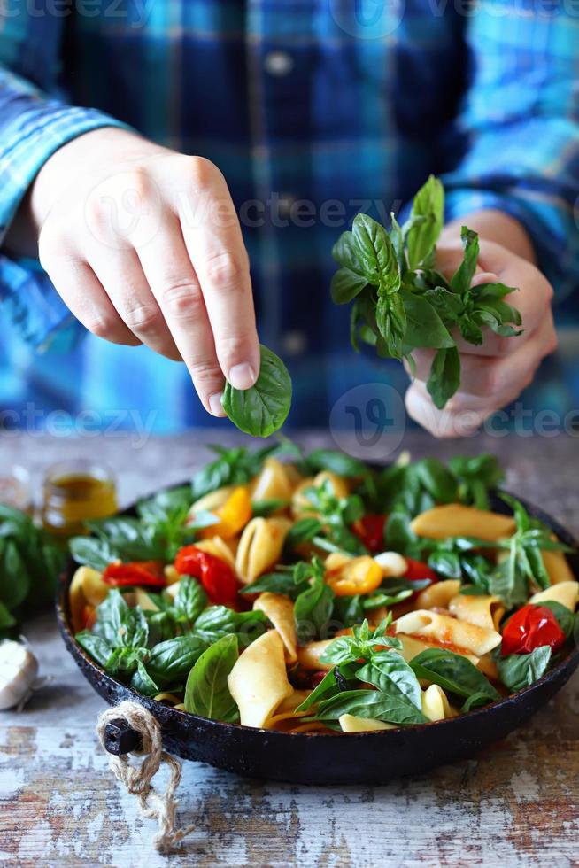 lo chef mescola la pasta con basilico e spezie in padella foto