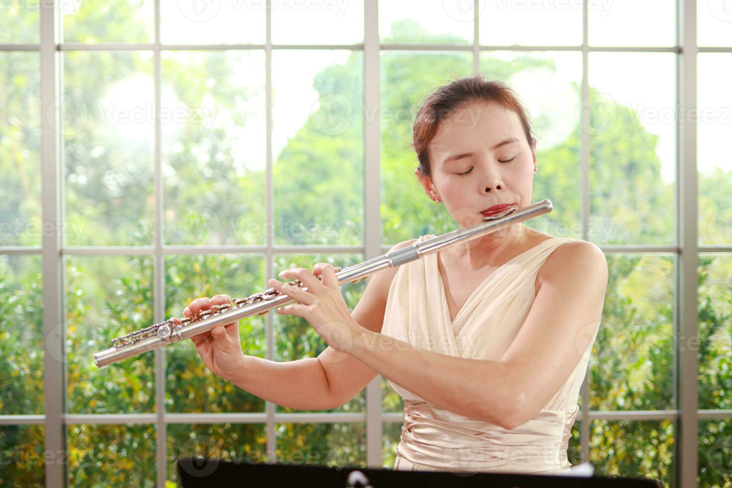 asiatico donna indossare un' crema colorato vestito lei è giocando il flauto, un internazionale vento strumento. giocare classico canzoni. l'esecuzione concerti giocando classico musica nel un' gruppo musicale. musica apprendimento foto