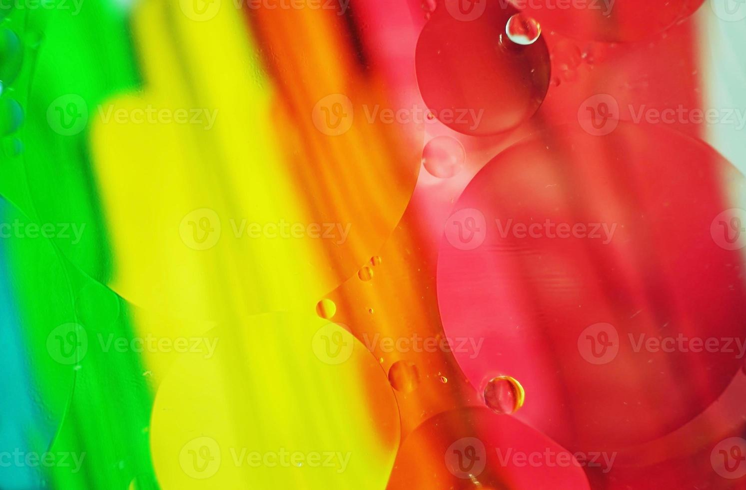 una bella e colorata macro di bolle d'olio sull'acqua con una trama a strisce gialle, rosse, verdi, arancioni e blu come motivo di sfondo foto