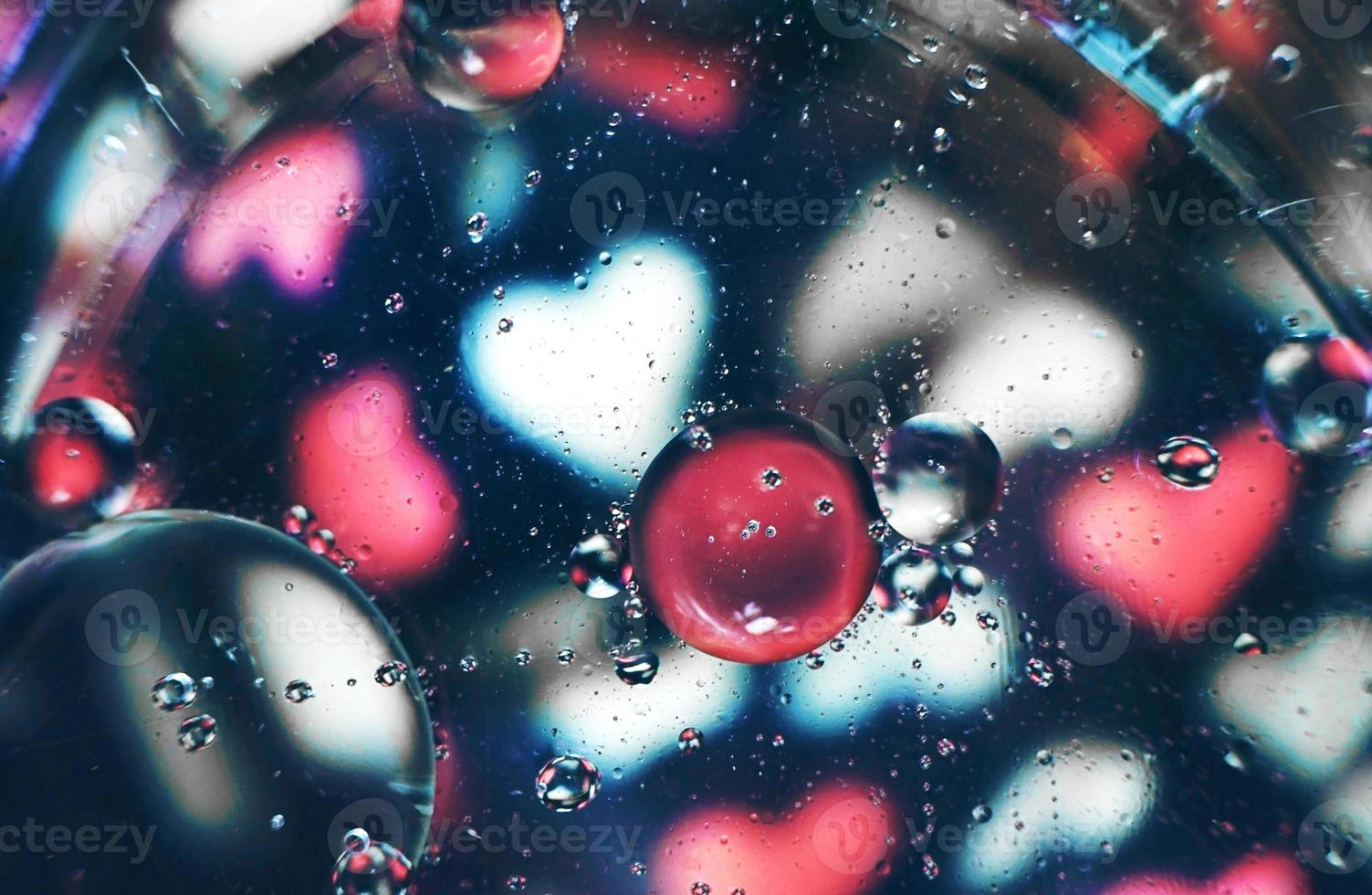 una bella e vibrante macro di bolle d'olio sull'acqua con una sfocatura di cuori bianchi e rosa su sfondo nero foto