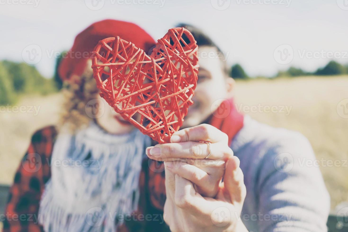 bel primo piano di un bel cuore rosso tenuto da una giovane coppia romantica innamorata in un bel bokeh come sfondo all'aperto. ricorda l'amore o l'assistenza sanitaria foto