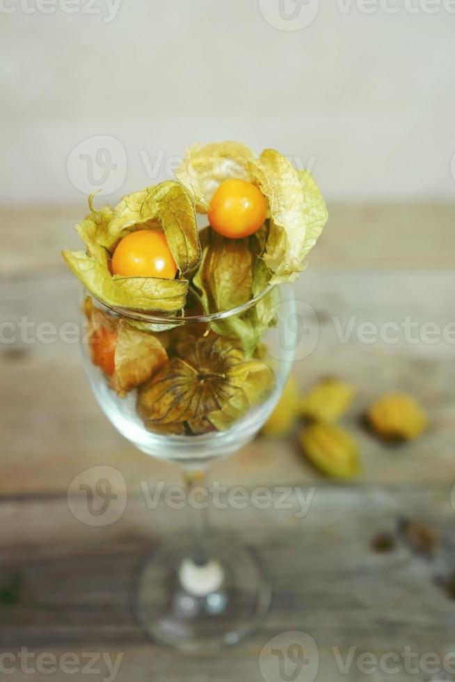 Bella ed elegante macro close-up di un sacco di frutta gustosa arancione denominata physalis dal Perù, Sud America, in un bicchiere di cristallo su tavoli di legno foto