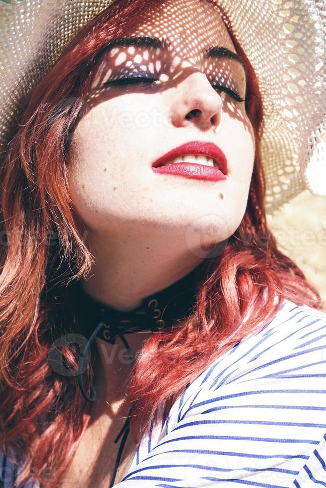 modella rossa che si protegge dal sole con un cappello in estate foto