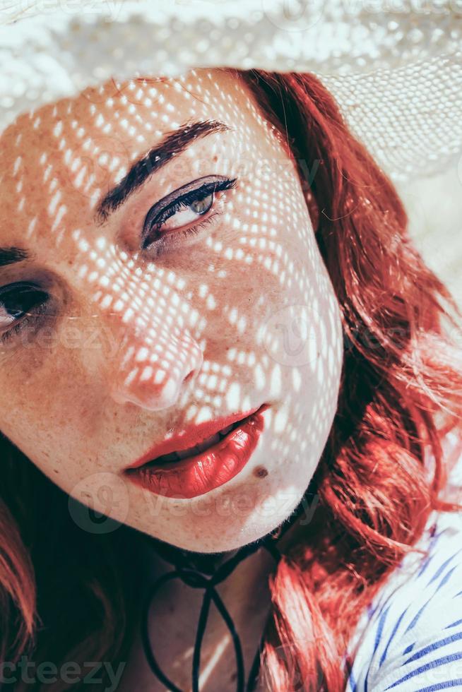 modella rossa che si protegge dal sole con un cappello in estate foto