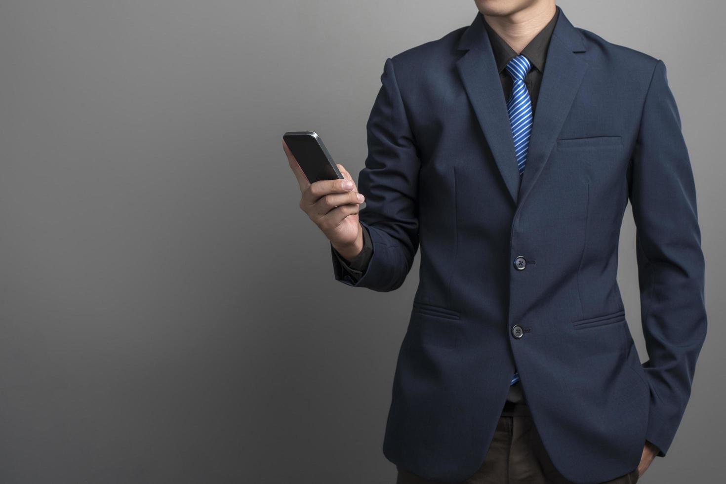 primo piano di uomo d'affari in abito blu che utilizza smartphone su sfondo grigio foto