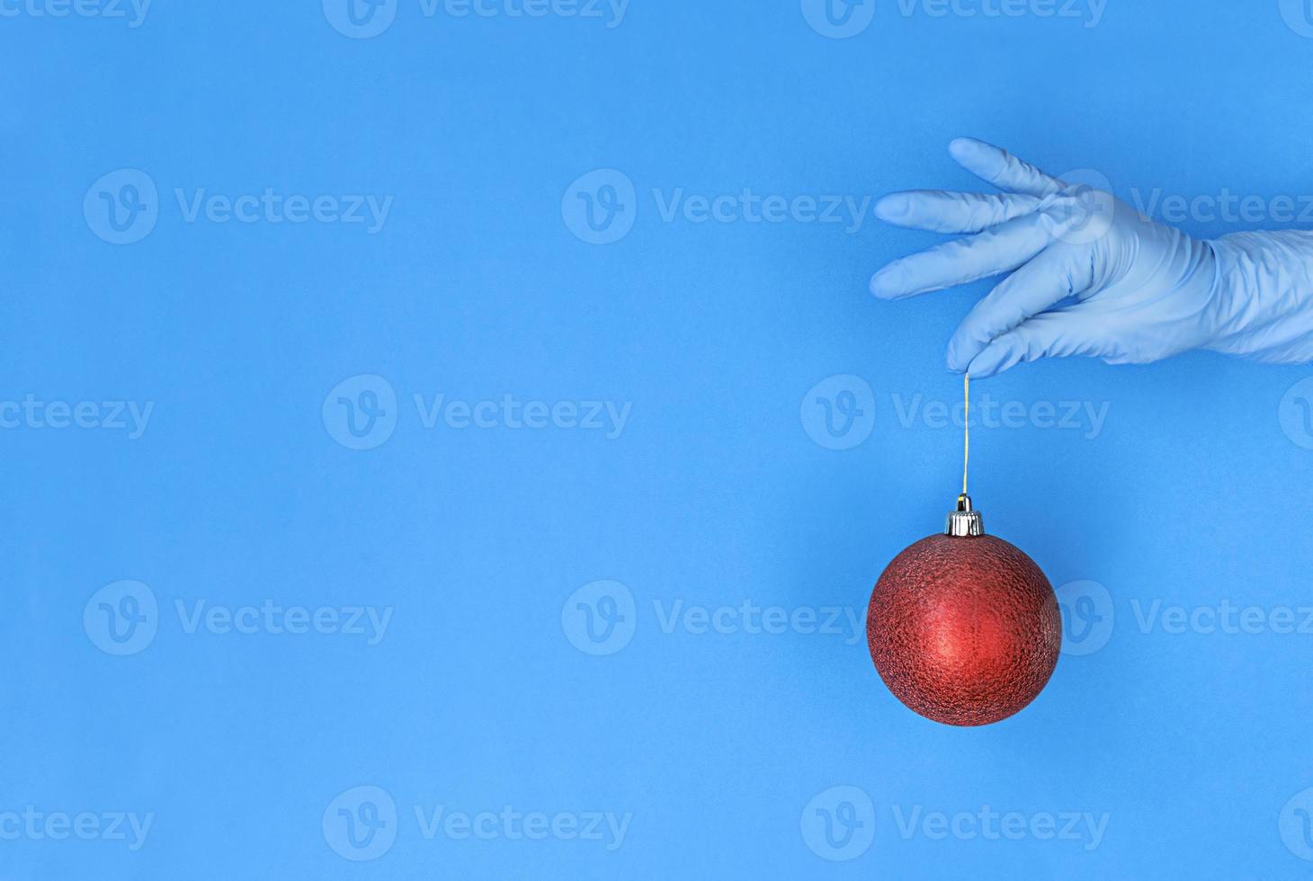 la mano in guanto medico tiene la palla rossa di natale su fondo blu con lo spazio della copia. foto