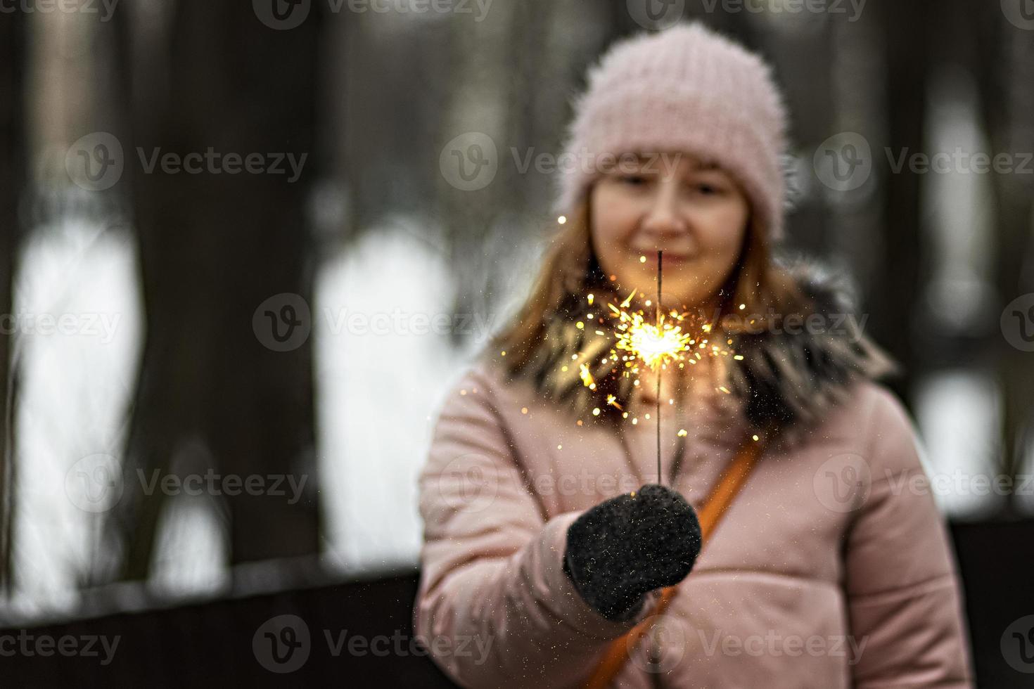 le luci di natale sono spruzzi luminosi che bruciano nelle mani di una donna felice e sfocata nel parco. scintillante. emozioni, umore del nuovo anno.vacanze invernali foto