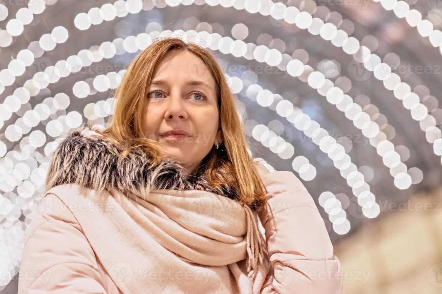 una bella giovane donna si trova in un centro commerciale con un bokeh di molte lampadine sullo sfondo. foto