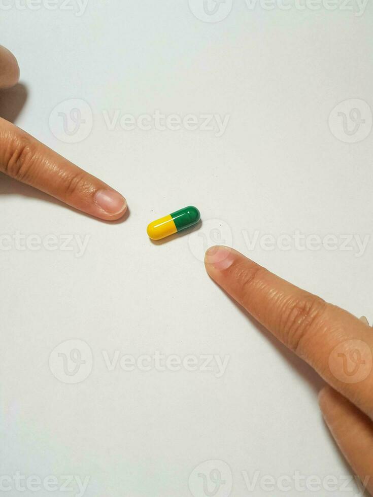 isolato bianca foto di Due indici puntamento a un' verde e giallo medicina capsula.