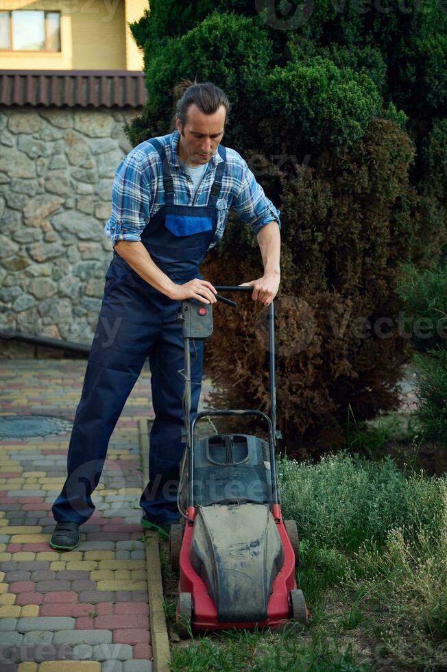 pieno lunghezza giardiniere Rifinitura erba prato utilizzando elettrico cordless tosaerba. paesaggio industria. giardino Manutenzione concetto foto