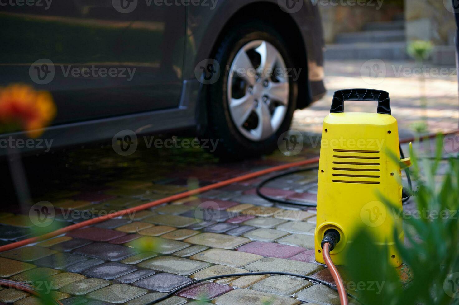 messa a fuoco su un' luminosa giallo auto pulizia attrezzatura vicino un' macchina. acqua alto pressione più pulito, rondella con tubo flessibile e spray bacchetta magica foto