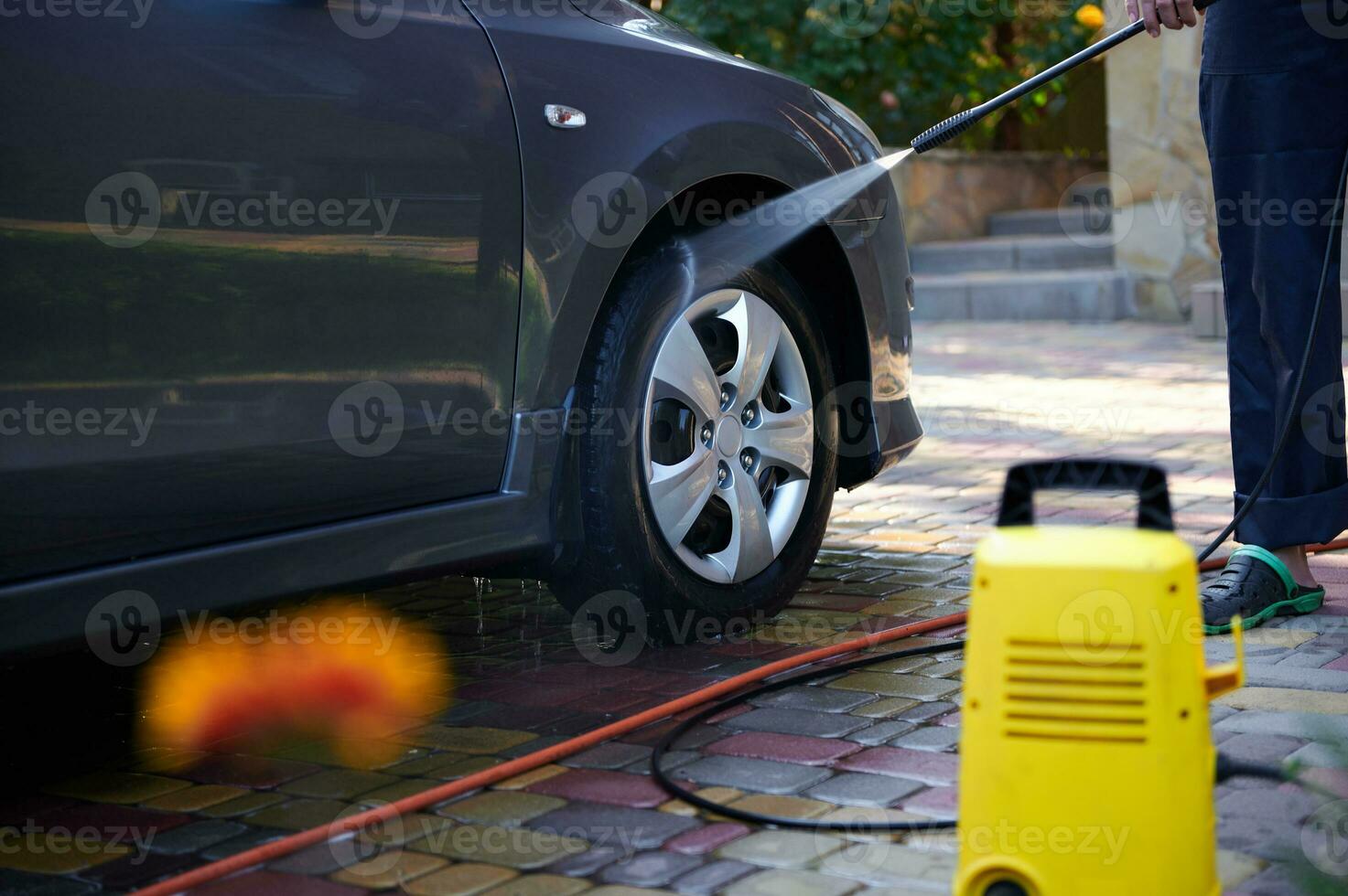 avvicinamento alto pressione acqua addetto alle pulizie come visto spruzzatura su auto ruota. uomo lavaggio auto all'aperto. automobile servizio concetto foto