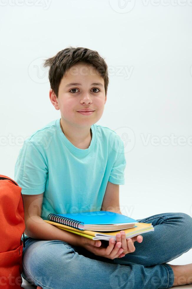 verticale studio ritratto di un' bello contento positivo scuola ragazzo ragazzo Tenere scuola forniture, sorridente guardare a telecamera foto