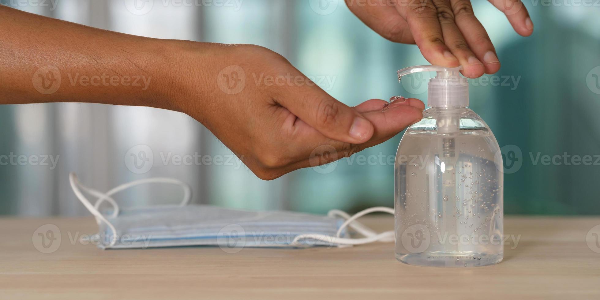 mano con disinfettante per le mani in gel alcolico e maschera medica sul tavolo foto