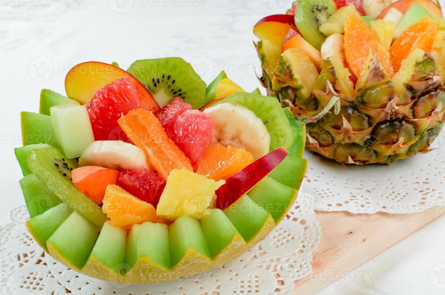 due macedonie di frutta fresca con kiwi, banana, pesca, arancia, arancia rossa, albicocca e melone in una ciotola di melone e ananas fatta a mano. foto