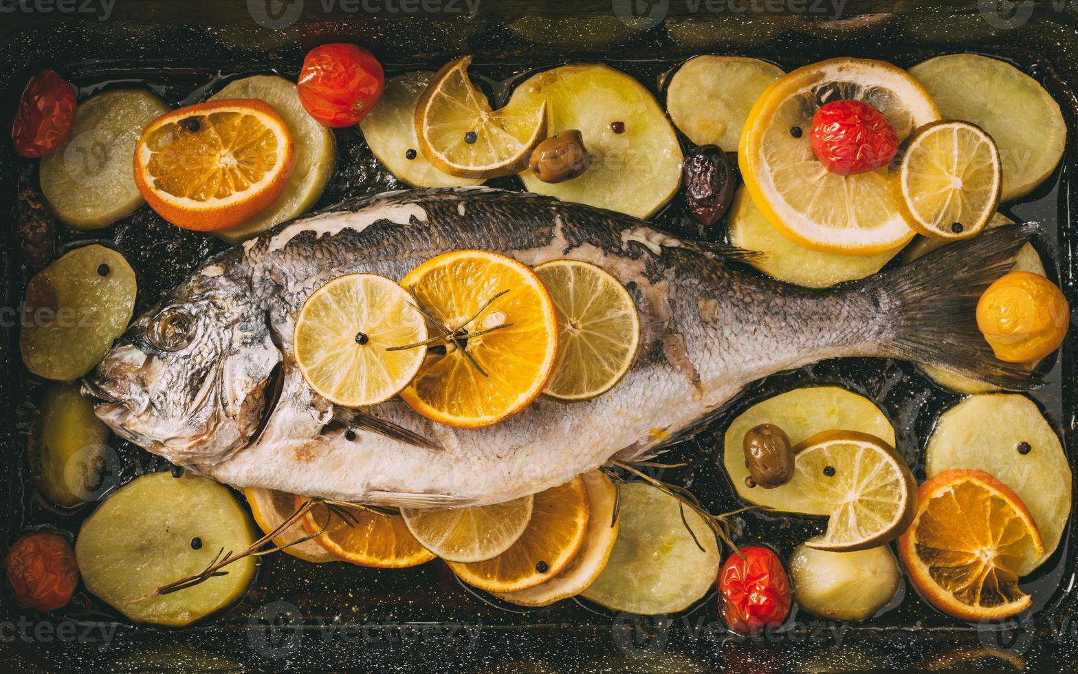 orata pesce in teglia al forno con patate, rosmarino, limone, arancia, olive, pomodori, cipolla e lime. orata fresca, preparazione di pesce dorade. foto