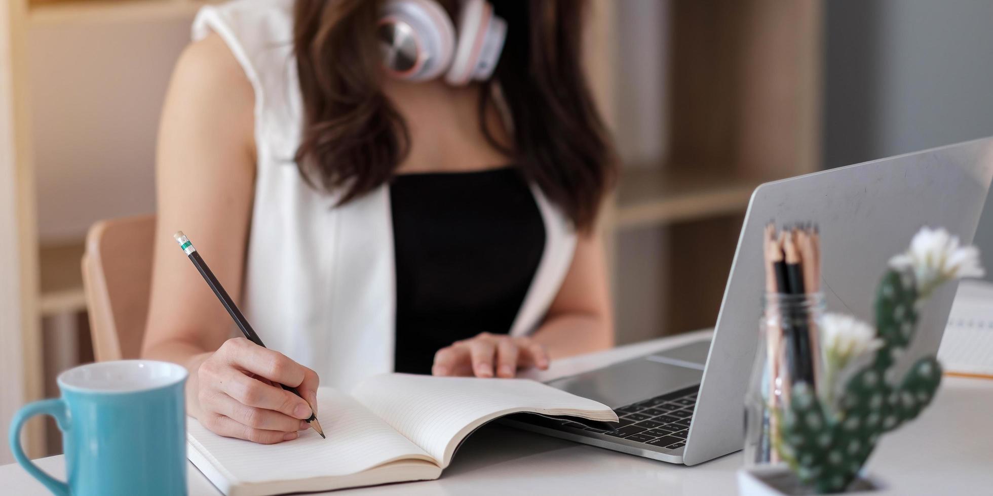 primo piano delle mani di una donna con computer portatile, notebook e penna per prendere appunti in ufficio foto