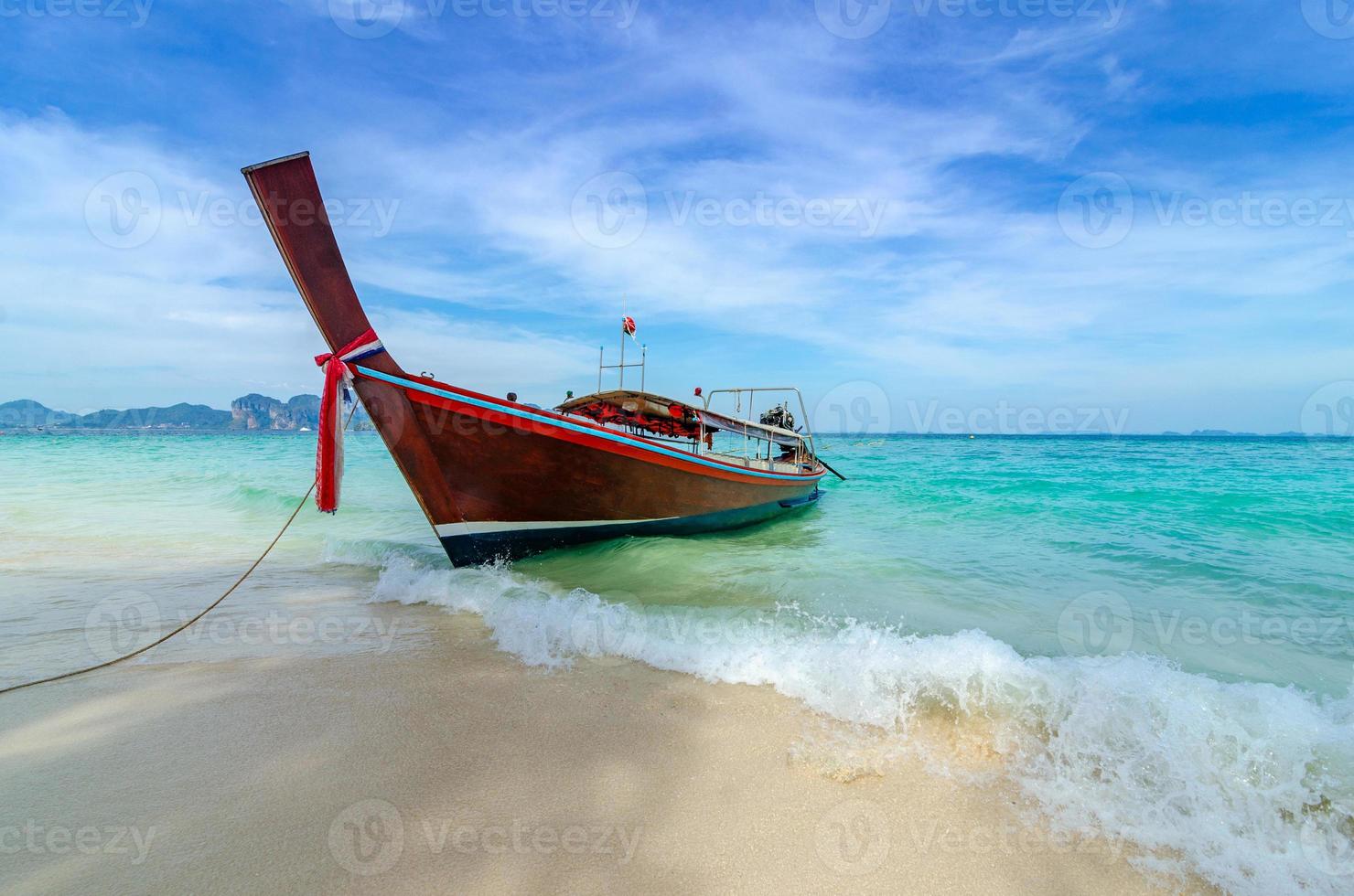 barca di legno parcheggiata sul mare, spiaggia bianca su un cielo azzurro e limpido, mare blu foto