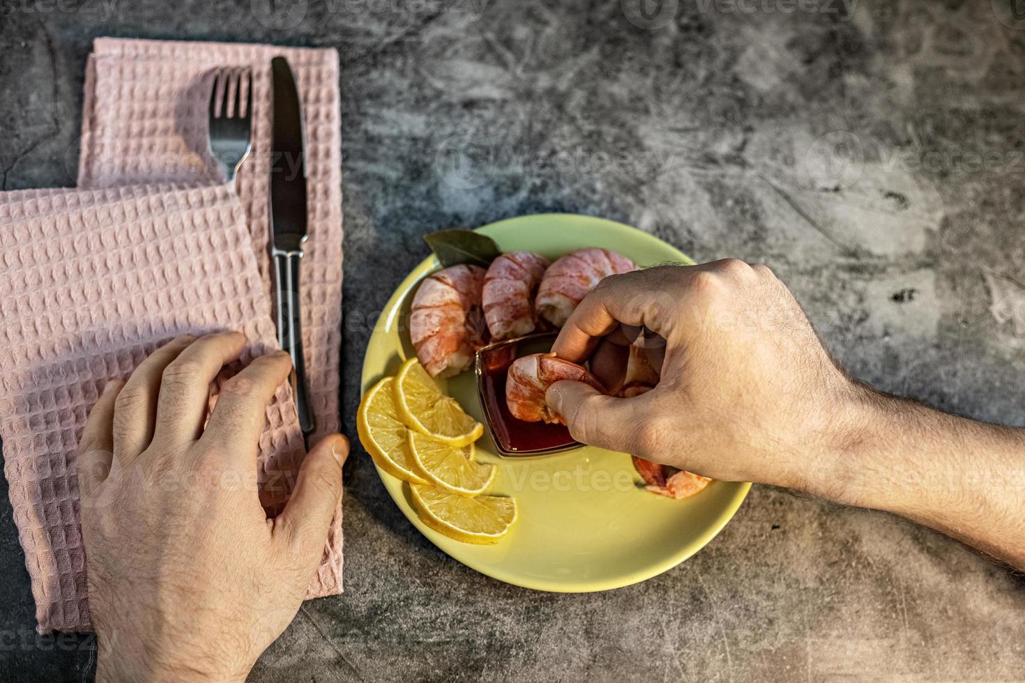 la mano di un uomo immerge un gambero reale in salsa di mirtilli rossi. il concetto di mangiar sano foto