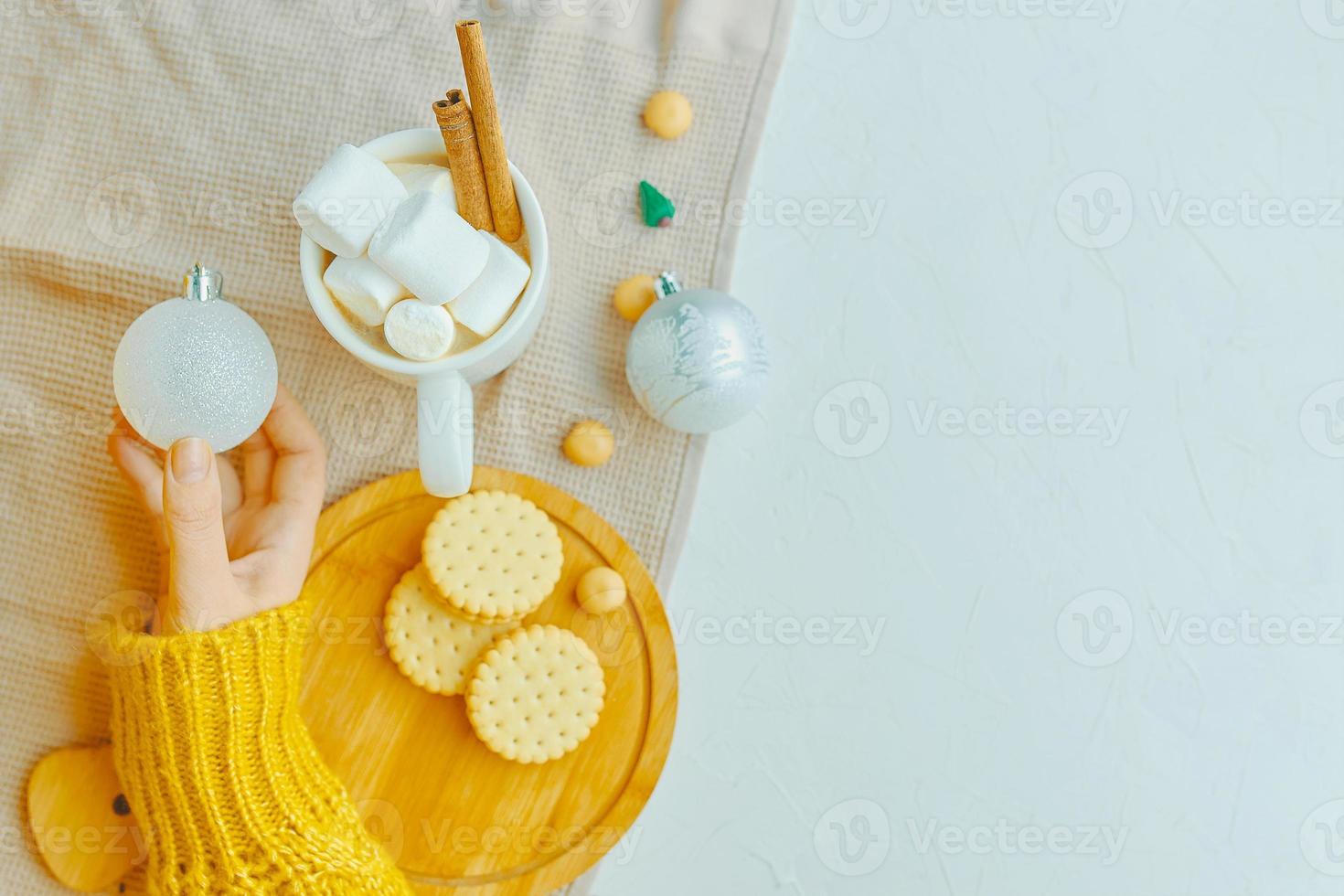 la ragazza tiene la palla di natale, la tazza di cacao, i biscotti e la tovaglia sul tavolo. foto