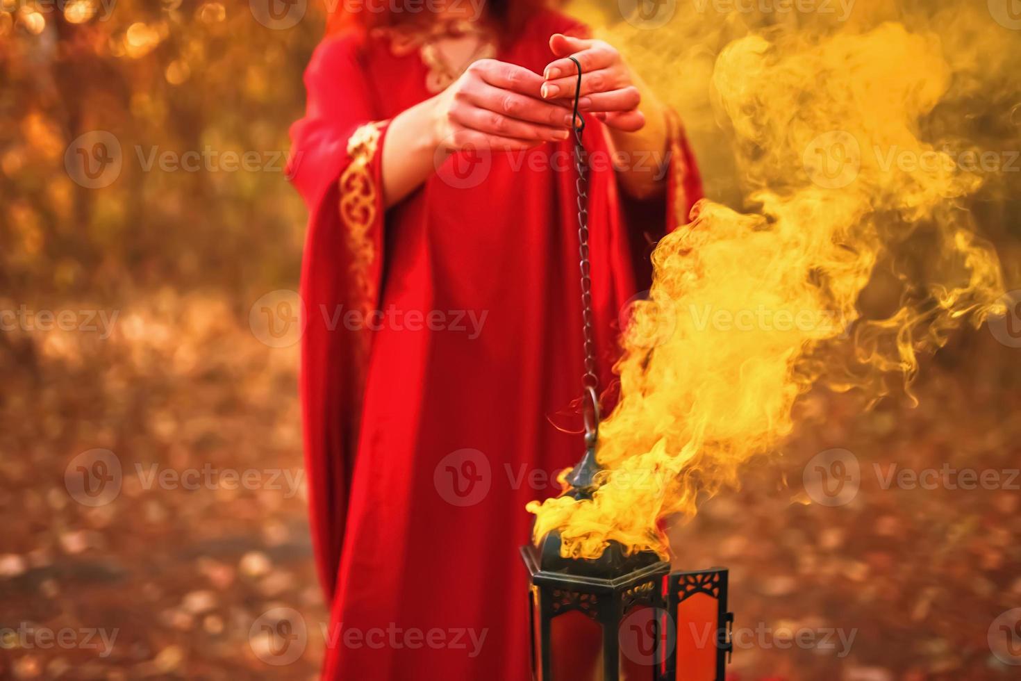 donna in una veste rossa tiene una lampada da cui esce fumo rosso foto