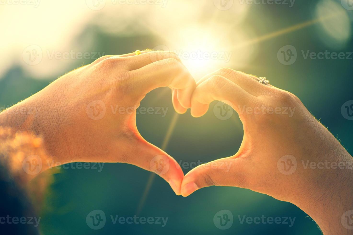 le mani delle donne e degli uomini sono a forma di cuore con la luce del sole che passa attraverso le mani foto
