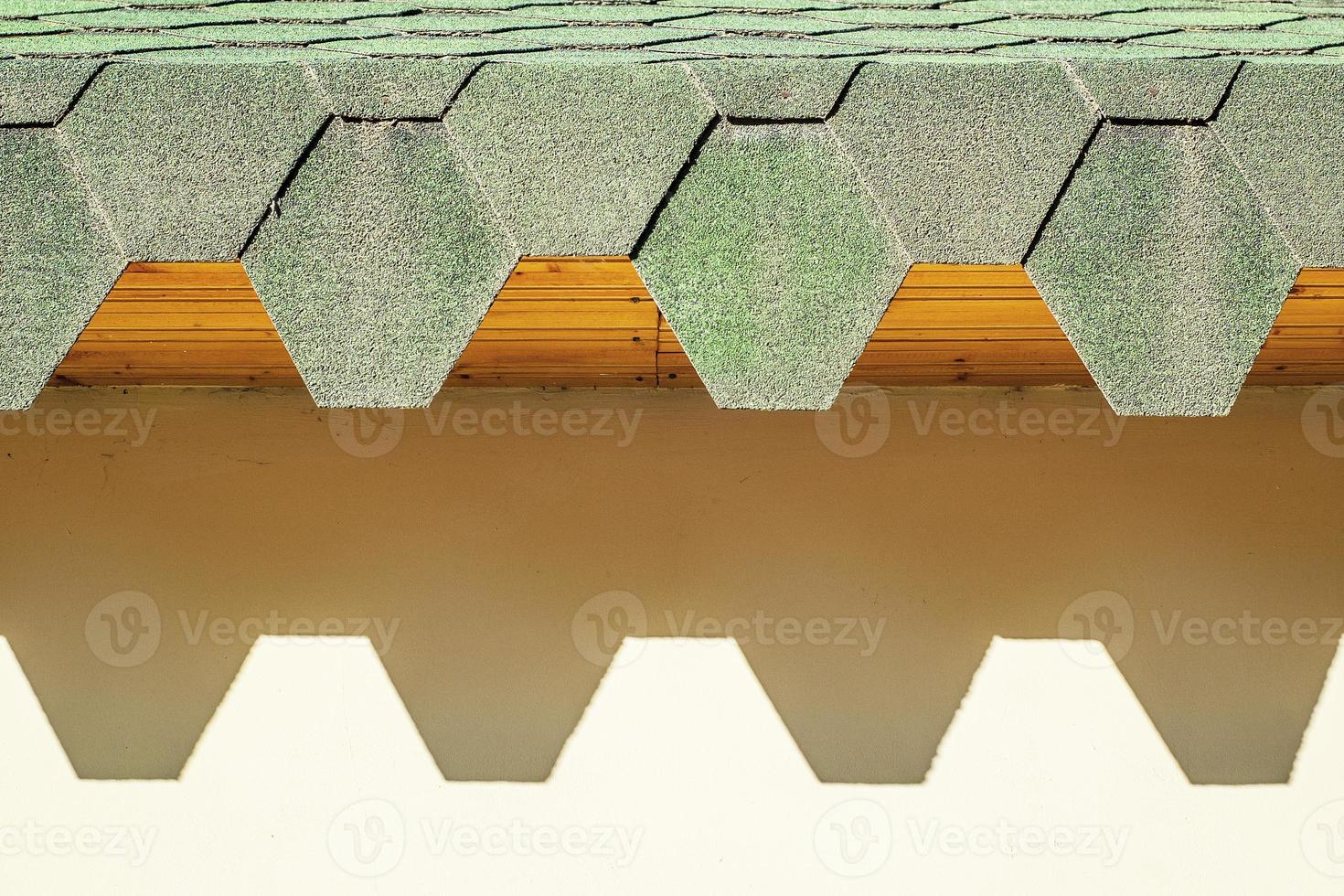 tetto verde con tegole esagonali. tetto con bordi frastagliati che proiettano ombre dure sul muro. foto