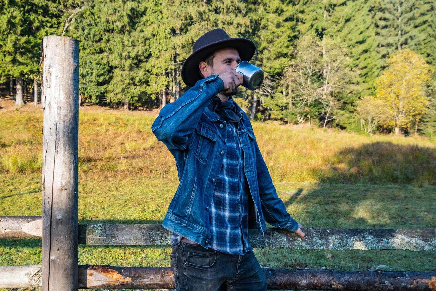 cowboy in giacca di jeans e cappello vicino al recinto in montagna foto