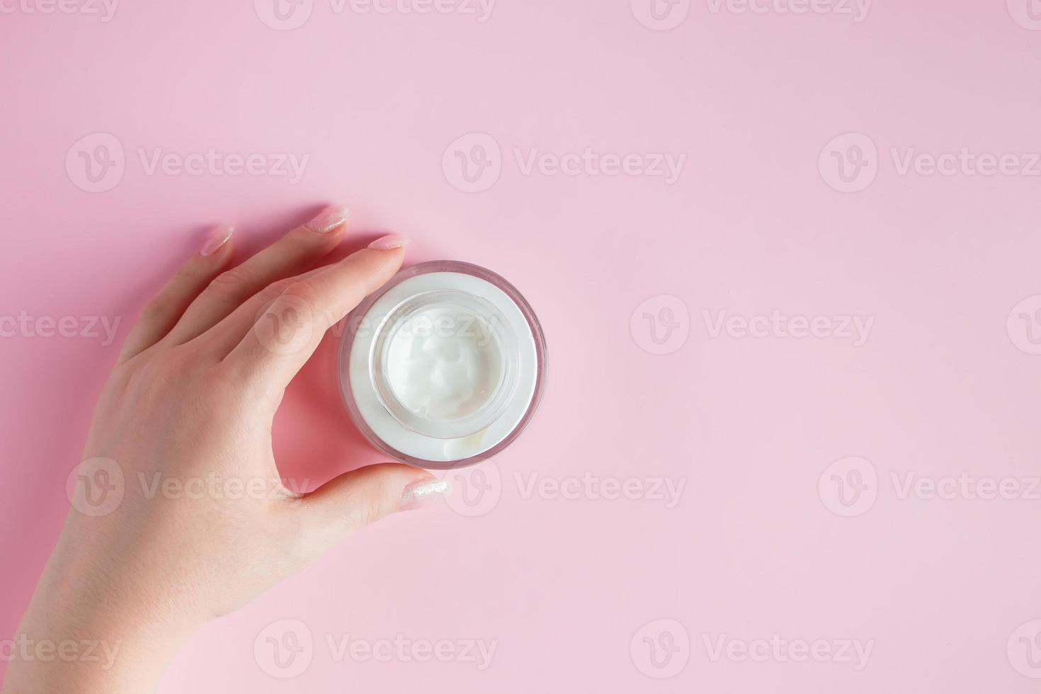 mani femminili con una bottiglia di crema su sfondo rosa. concetto di spa e cura del corpo. immagine per la pubblicità foto