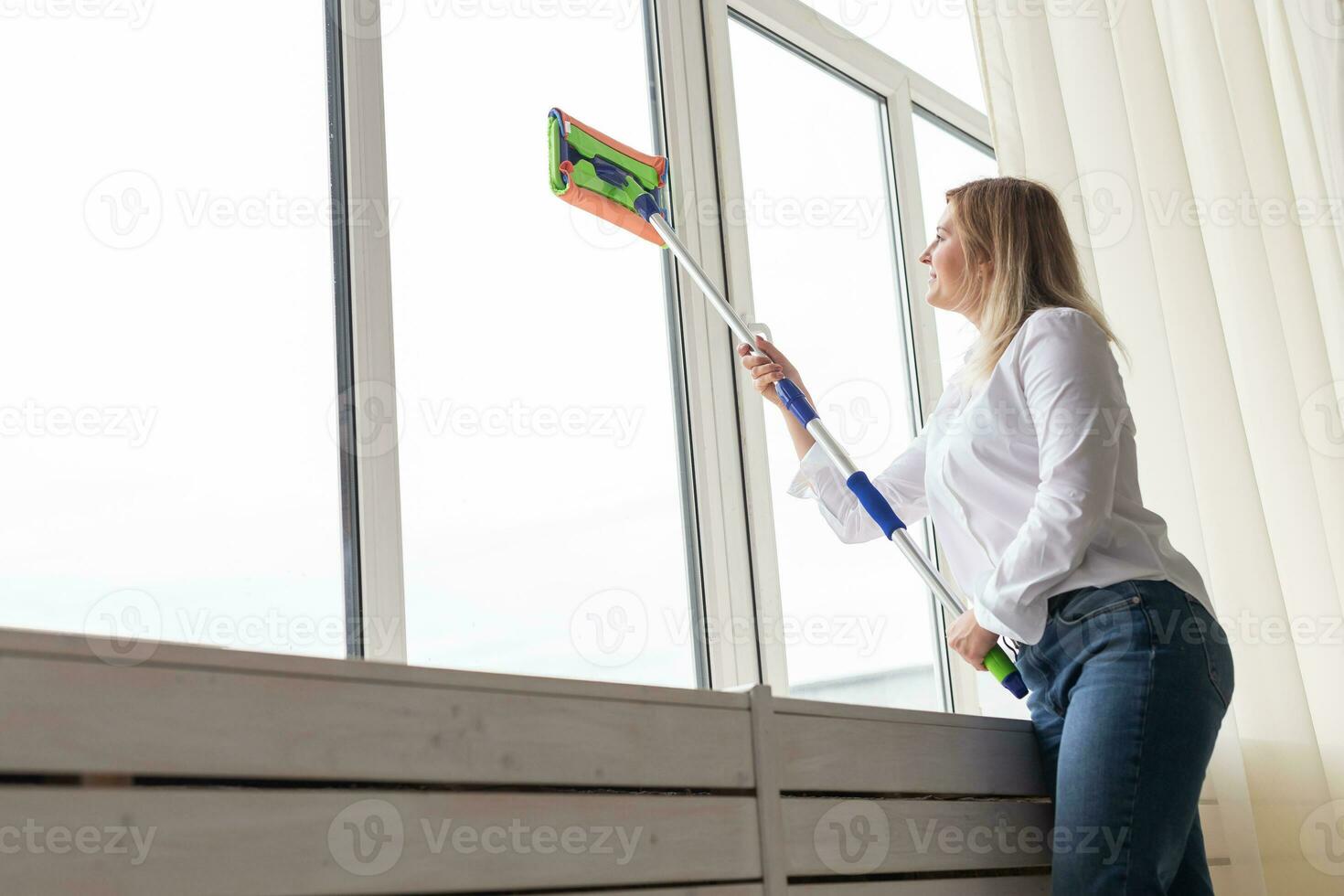 contento donna pulizia finestra con spugna Mocio a casa - lavori di casa e faccende domestiche concetto foto