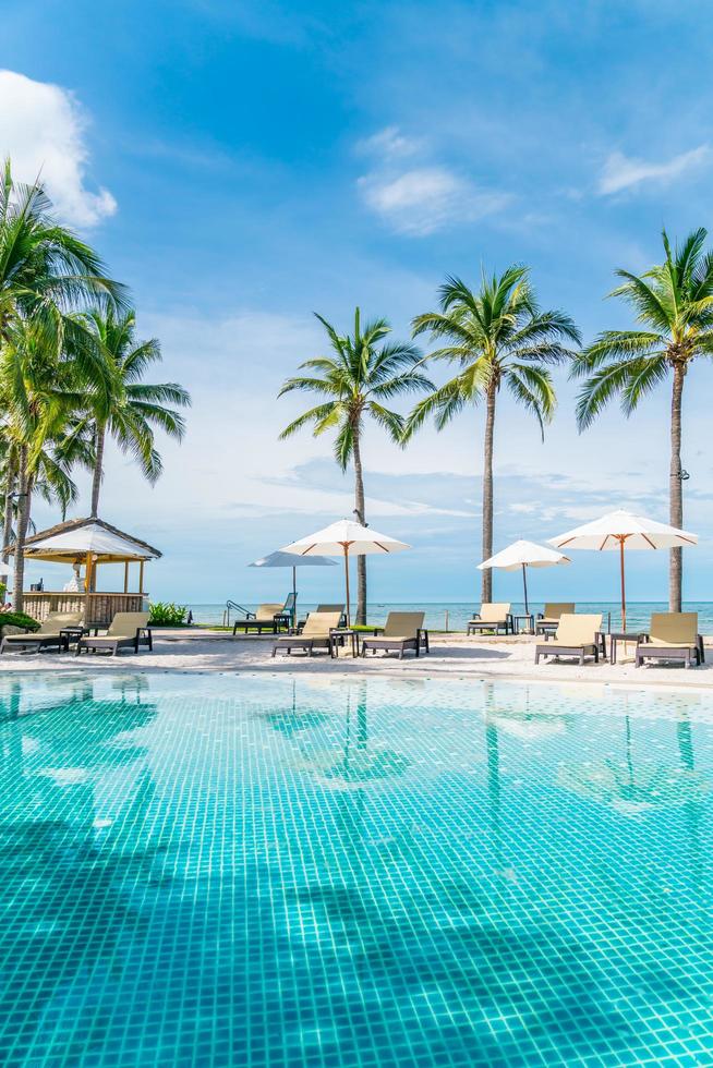 bellissima spiaggia tropicale e mare con ombrellone e sedia intorno alla piscina nel resort dell'hotel foto