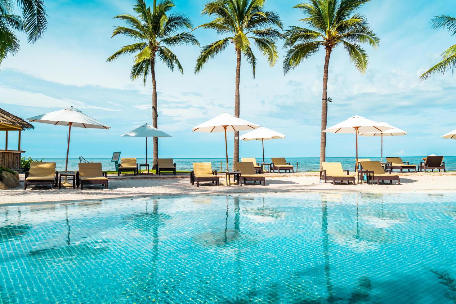 bellissima spiaggia tropicale e mare con ombrellone e sedia intorno alla piscina nel resort dell'hotel foto