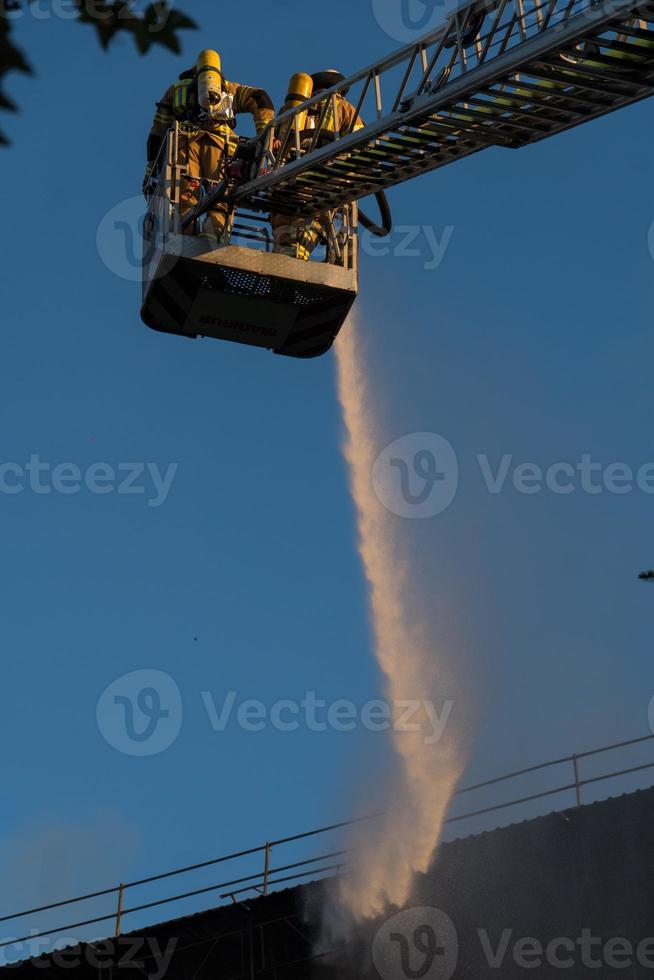 vigili del fuoco che salgono la scala contro la costruzione e l'estinzione di un incendio foto