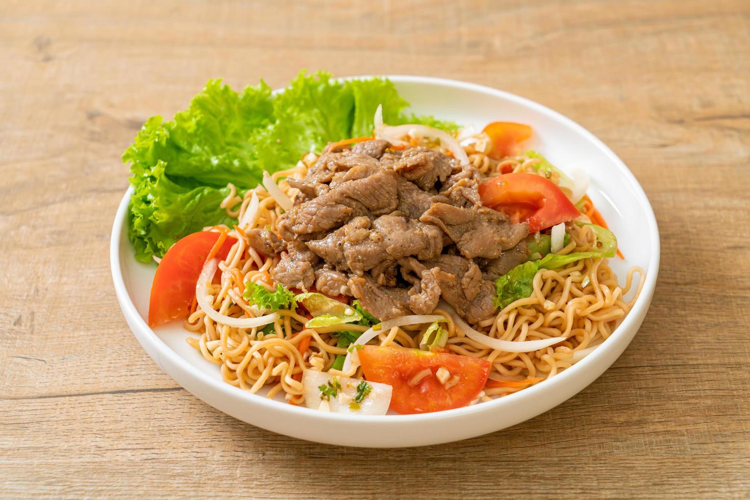 Insalata piccante di noodle istantanei con carne di maiale su un piatto bianco - stile cibo asiatico foto