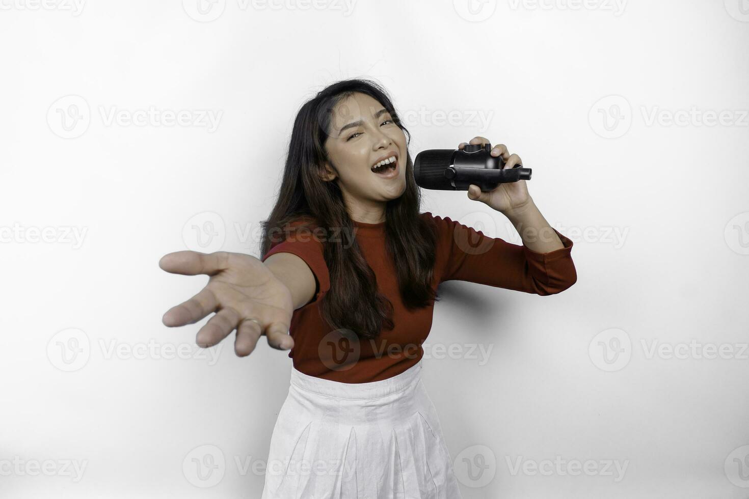 ritratto di spensierato asiatico donna, avendo divertimento karaoke, cantando nel microfono mentre in piedi al di sopra di bianca sfondo foto