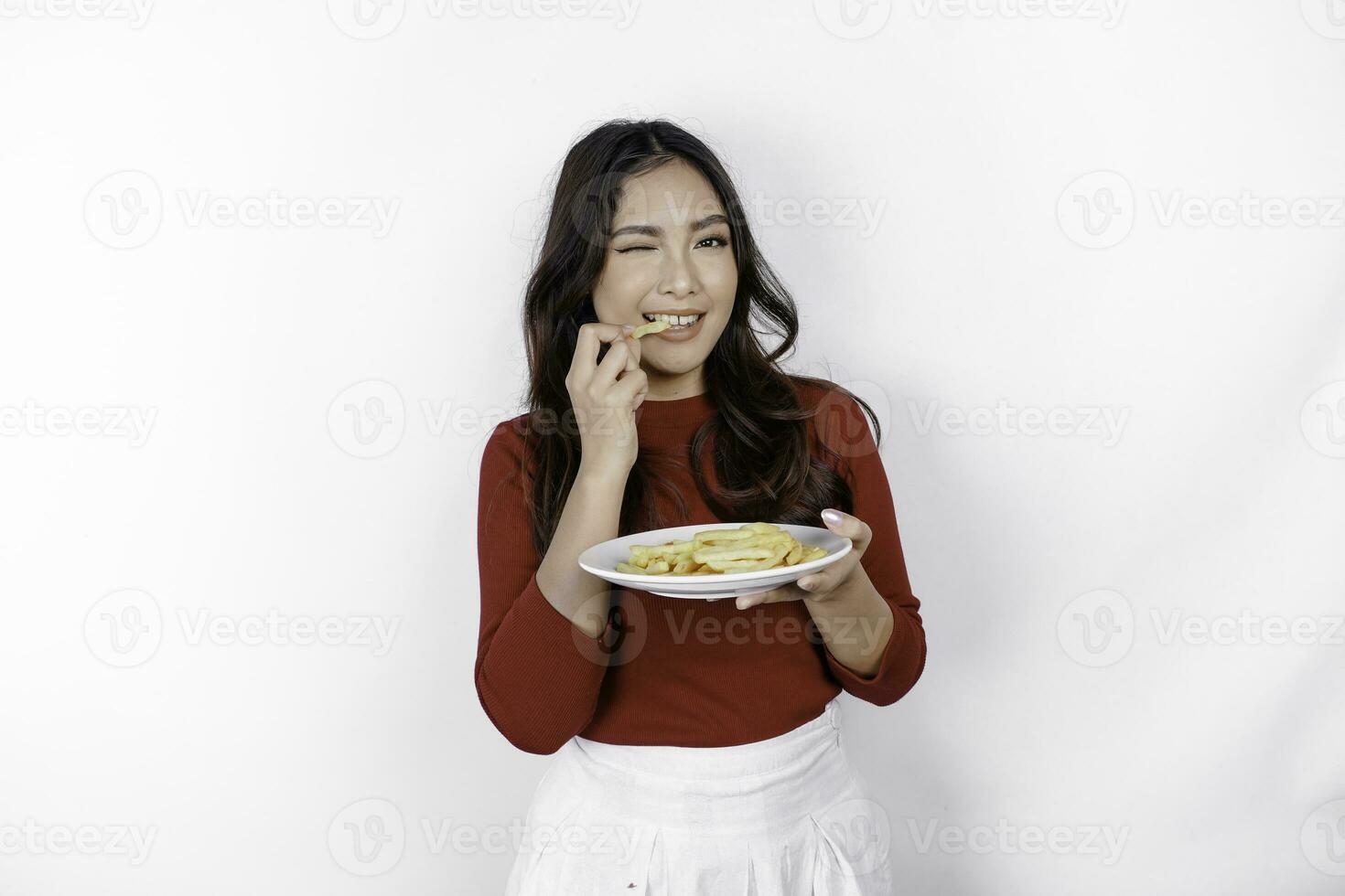 Immagine di sorridente giovane asiatico ragazza mangiare francese patatine fritte isolato su bianca sfondo foto