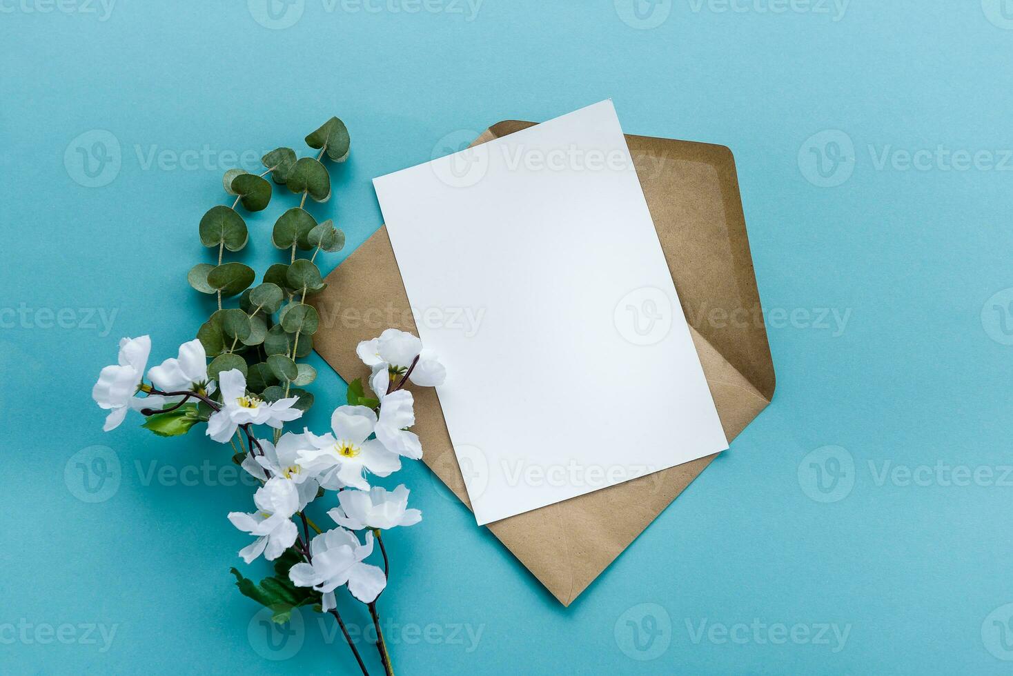 un' kraft carta Busta con un' bianca vuoto carta fiori su un' blu sfondo. cartolina preparazione foto