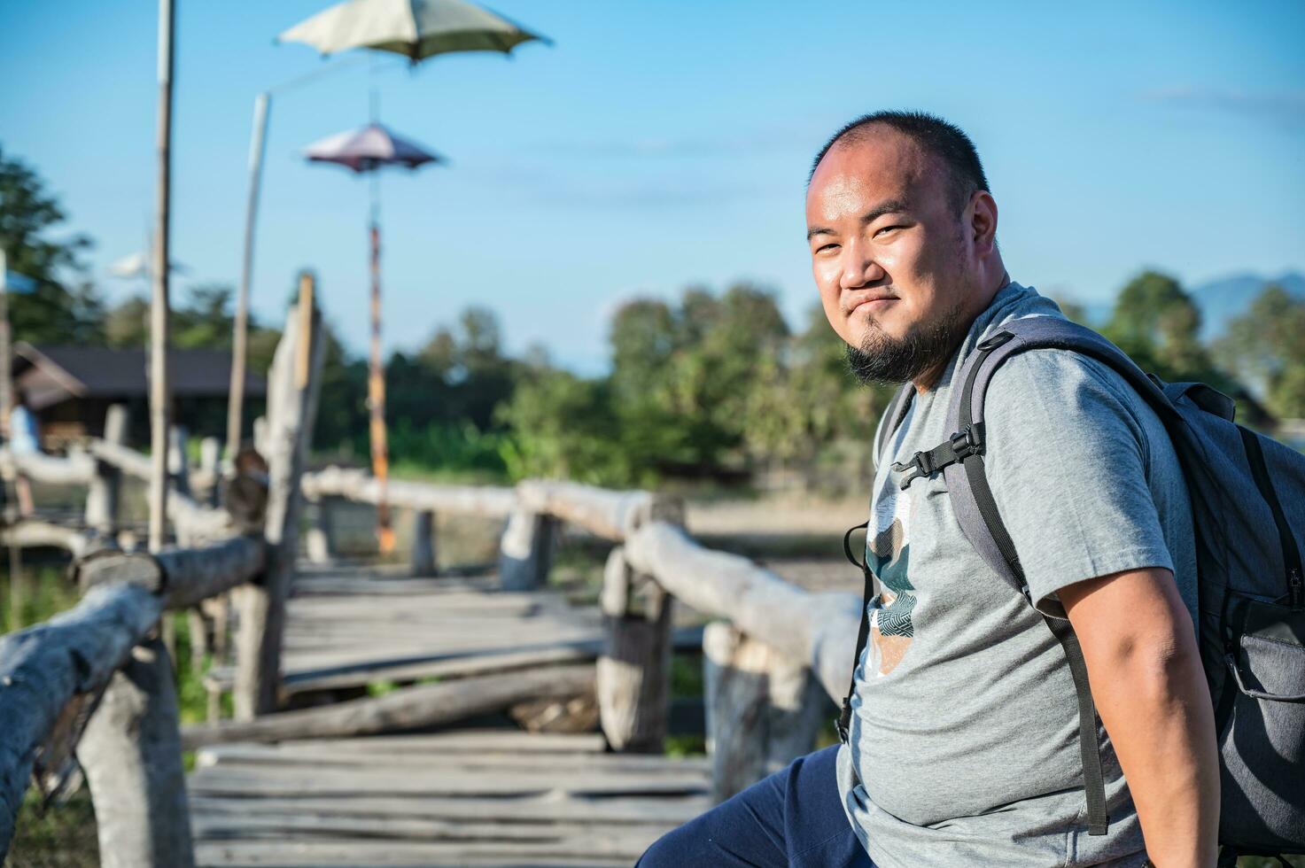 asiatico zaino in spalla Grasso uomo con barba su il di legno ponte con blu cielo nel vacanza tempo foto