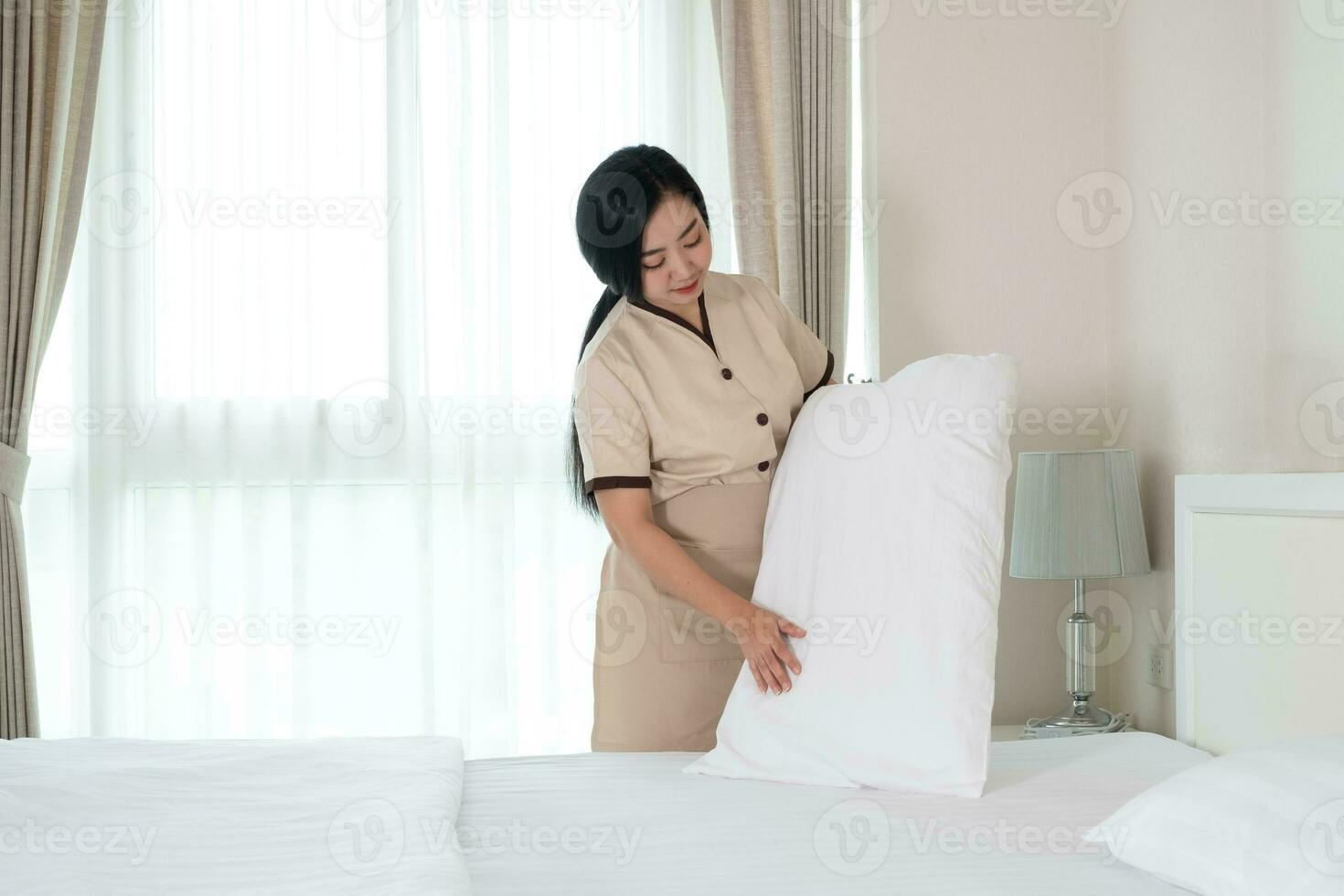 giovane bella cameriera asiatica che sistema un cuscino sul letto in una stanza d'albergo. foto