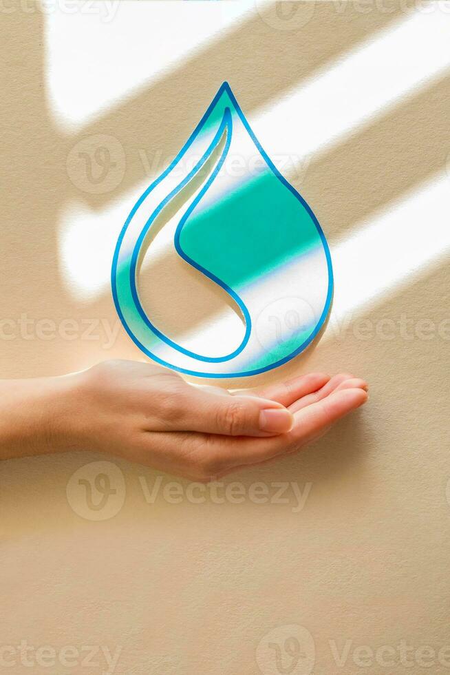 donna mano Tenere carta tagliare acqua far cadere su beige sfondo. pulito acqua e servizi igienico-sanitari, Salvataggio acqua. mondo acqua giorno. ecologia concetto. foto