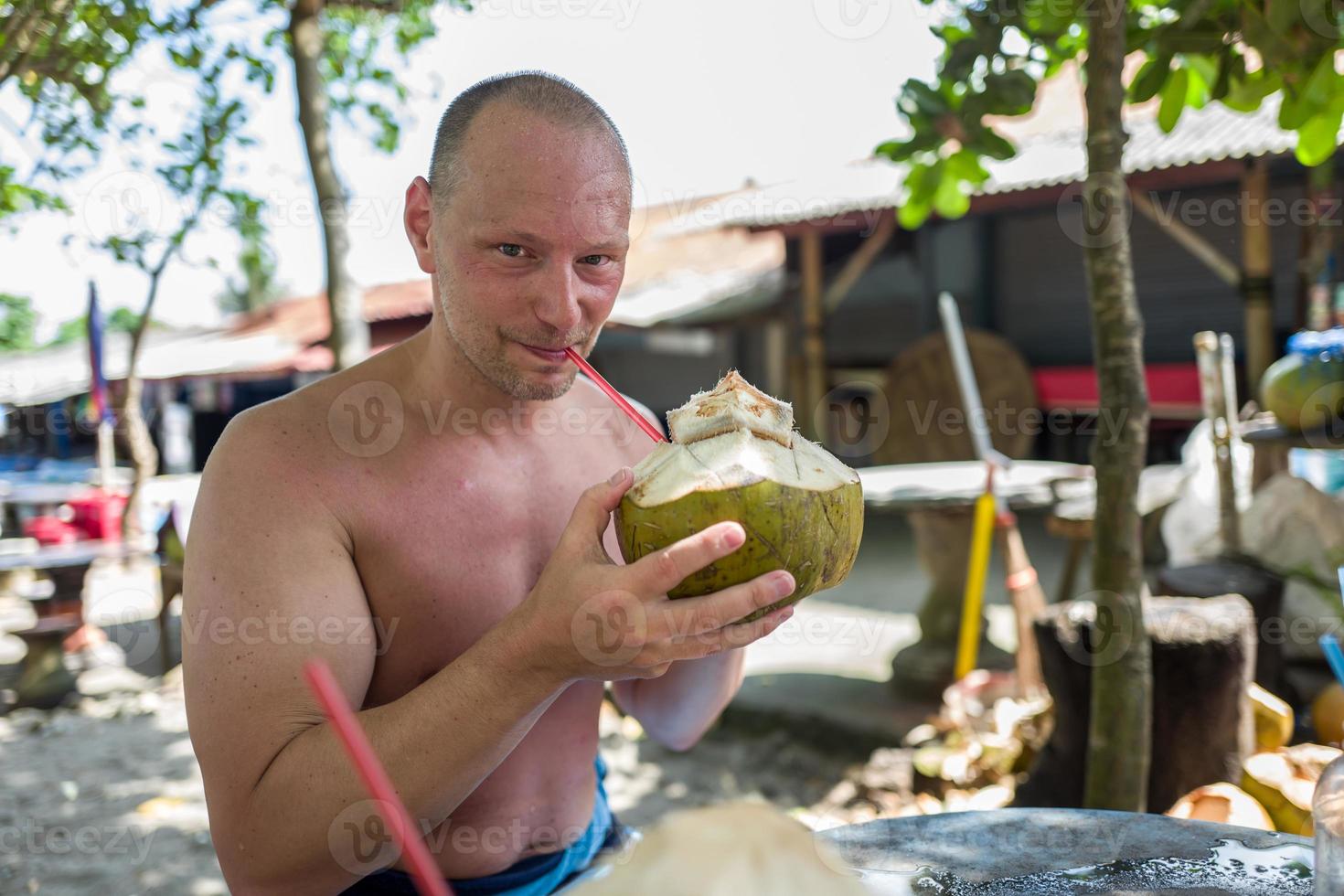 Uomo caucasico che beve dalla noce di cocco a Echo Beach a Bali foto